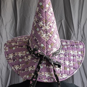 May include: A purple witch hat with a black ribbon and a print of potion bottles. The hat is quilted and has a pointed crown. The text "VIEW TWO: QUILTED NON PATCHWORK" is visible in the image.