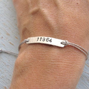 Pode incluir: Uma pulseira de prata com um cord&atilde;o cinza e uma etiqueta de prata que diz "11964".