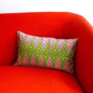 May include: A red sofa with a green and pink patterned pillow. The pillow has a geometric design with triangles and floral accents.