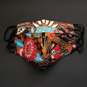 May include: A black face mask with a colorful floral pattern in shades of red, blue, orange, and white. The mask is made of fabric and has elastic ear loops.