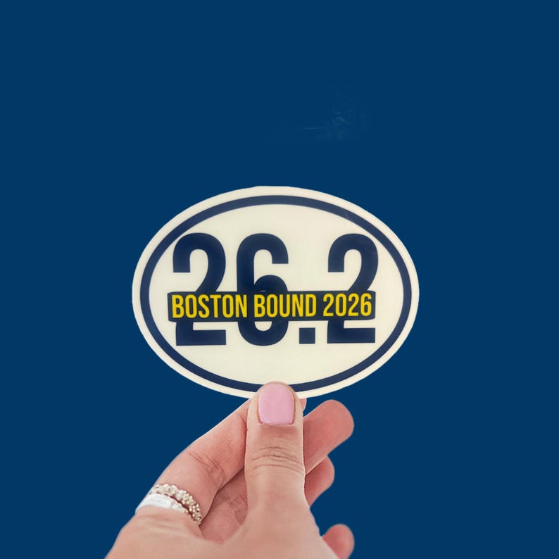 Puede incluir: Una pegatina ovalada con el texto "26.2" en azul marino, con "BOSTON BOUND 2026" en amarillo. La pegatina est&aacute; sobre un fondo azul oscuro. La pegatina es un art&iacute;culo tem&aacute;tico de marat&oacute;n.