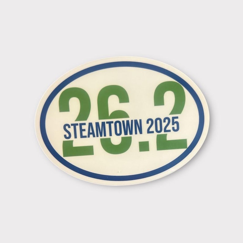 Puede incluir: Adhesivo ovalado con el texto "26.2 STEAMTOWN 2025" en verde y azul. El adhesivo tiene un fondo crema con un borde azul y verde. El dise&ntilde;o es simple y audaz, para corredores de marat&oacute;n.