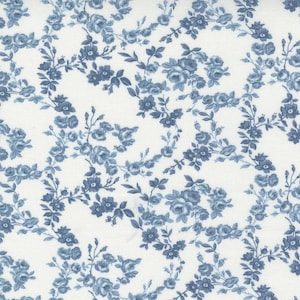 May include: A close-up of a white fabric with a repeating pattern of blue floral vines and blossoms. The flowers are detailed with multiple petals and leaves, creating a classic, vintage aesthetic. The design is suitable for quilting or crafting.
