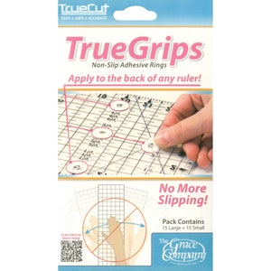Pode incluir: Embalagem de anéis adesivos antiderrapantes TrueGrips. A embalagem apresenta o texto "TrueGrips" em rosa e "Non-Slip Adhesive Rings" abaixo. A imagem mostra os anéis sendo aplicados a uma régua. A embalagem contém 15 anéis grandes e 15 pequenos.