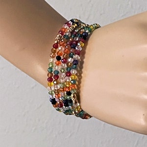 May include: Multicolored crystal bead bracelet with a woven design. The bracelet features shades of red, orange, yellow, green, blue, and black.