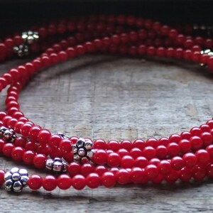 Puede incluir: Un collar de m&uacute;ltiples hilos hecho de cuentas rojas con acentos de flores plateadas.