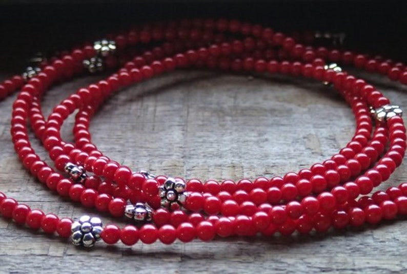 Puede incluir: Un collar de m&uacute;ltiples hilos hecho de cuentas rojas con acentos de flores plateadas.
