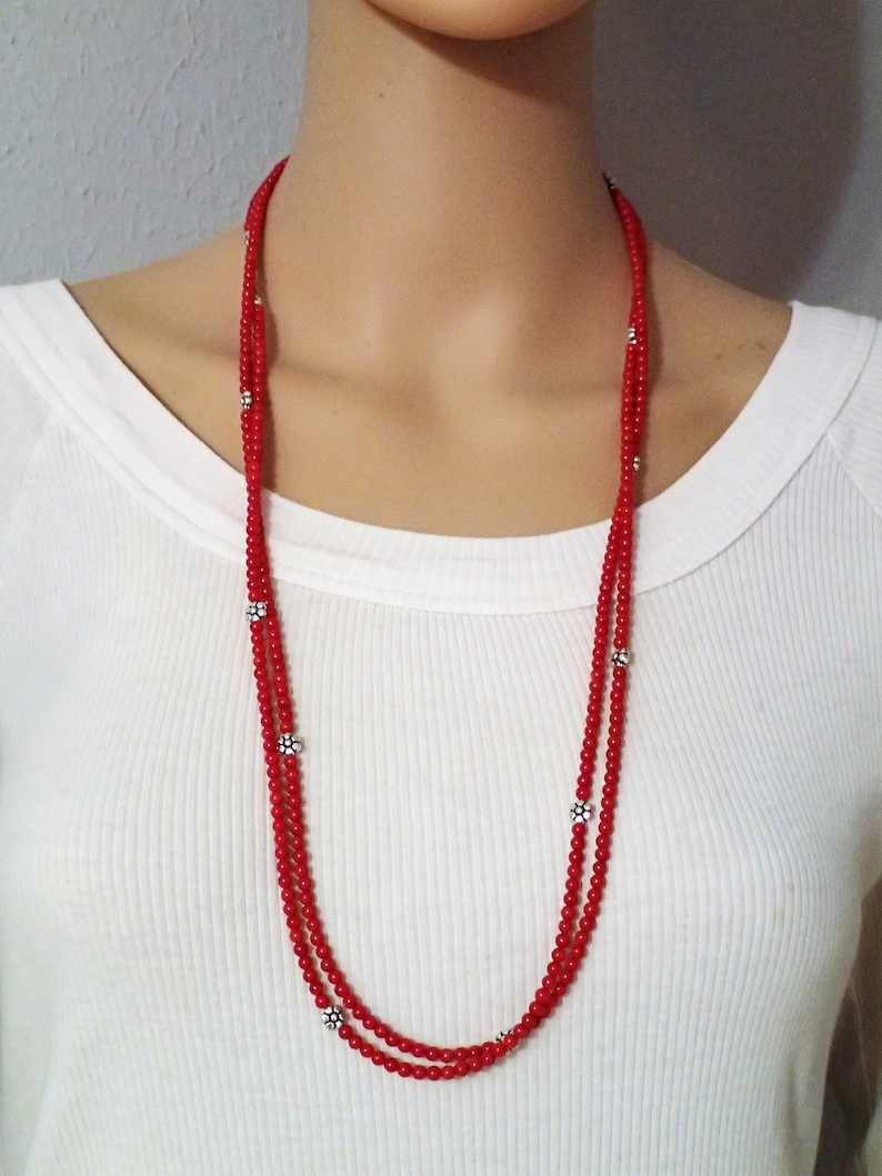 Puede incluir: Un collar de doble cadena hecho de cuentas rojas con acentos de flores plateadas.