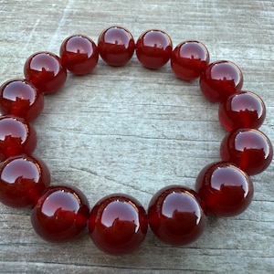 May include: A circular arrangement of large, polished, deep red beads. The beads are evenly spaced, creating a continuous loop. The glossy surface of each bead reflects light, enhancing their rich color and smooth texture. The beads are likely part of a necklace or bracelet.