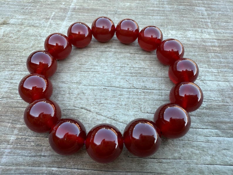 May include: A circular arrangement of large, polished, deep red beads. The beads are evenly spaced, creating a continuous loop. The glossy surface of each bead reflects light, enhancing their rich color and smooth texture. The beads are likely part of a necklace or bracelet.