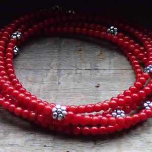Puede incluir: Un collar de m&uacute;ltiples hilos hecho de cuentas de coral rojo con acentos de plata en forma de flor.