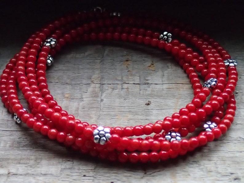 Puede incluir: Un collar de m&uacute;ltiples hilos hecho de cuentas de coral rojo con acentos de plata en forma de flor.