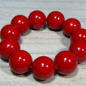 May include: A red beaded bracelet with 10 round beads. The beads are glossy and smooth.