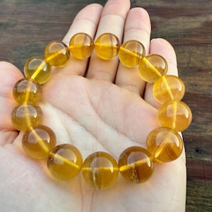 May include: A bracelet made of large, round, amber-colored beads. The beads are strung together, forming a circular shape. The bracelet is held in a hand, with the beads appearing to be approximately 1 inch in diameter.