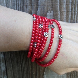 Puede incluir: Un brazalete de cuentas rojas con detalles de flores plateadas. El brazalete est&aacute; envuelto varias veces alrededor de una mu&ntilde;eca.