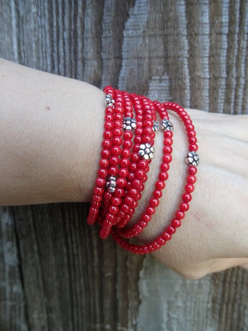 Puede incluir: Un brazalete de cuentas rojas con detalles de flores plateadas. El brazalete est&aacute; envuelto varias veces alrededor de una mu&ntilde;eca.