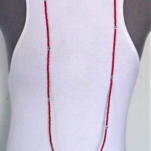 Puede incluir: Un collar largo de cuentas rojas con detalles en forma de flor plateados. El collar est&aacute; superpuesto dos veces, creando una longitud m&aacute;s larga.