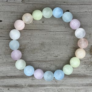 May include: A bracelet made of round, pastel-colored beads. The beads are in shades of pink, blue, green, and white. The bracelet is displayed on a weathered wooden surface.