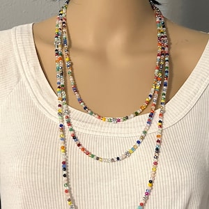 May include: A multi-strand necklace made of colorful glass beads. The beads are small and round, and they are arranged in a random pattern. The necklace is long and can be worn in a variety of ways.