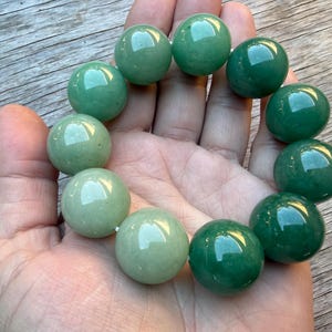 May include: A stretch bracelet composed of large, smooth, spherical beads in varying shades of green, ranging from light mint to deep forest green, arranged in a circular pattern with a polished, reflective surface finish.