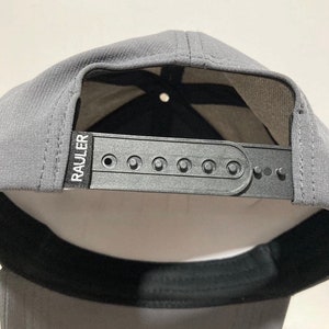 May include: A grey baseball cap with a black adjustable strap and the word "RAULER" printed in white on the strap.