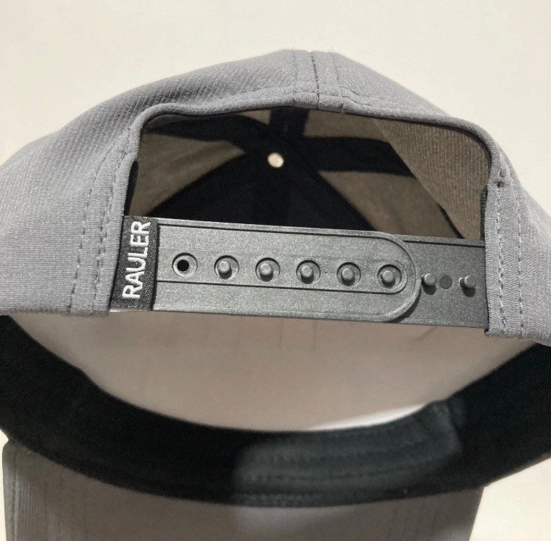 May include: A grey baseball cap with a black adjustable strap and the word "RAULER" printed in white on the strap.
