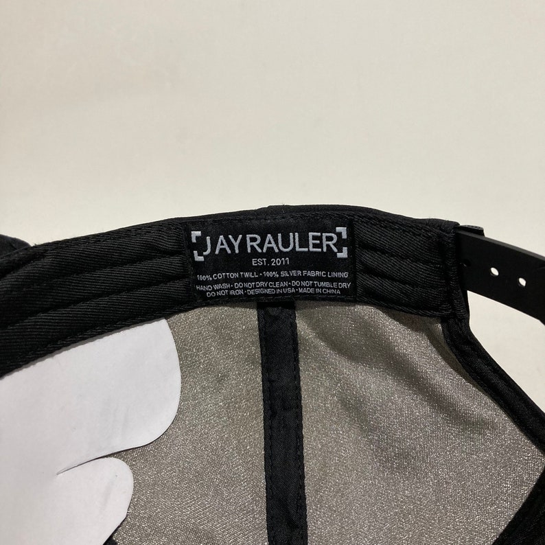 May include: Black baseball cap with a white label that reads "JAY RAULER EST. 2011" and includes care instructions. The label is sewn onto the inside of the cap.