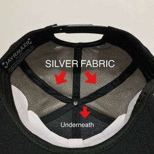 May include: Inside view of a black baseball cap with a white underside. The cap has a black strap and a silver fabric lining. The text "SILVER FABRIC" is printed on the lining, with arrows pointing to the fabric. The text "Underneath" is printed below the arrows.