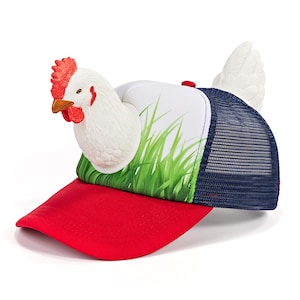 May include: A trucker hat featuring a red brim and a white front panel printed with green grass. A three-dimensional white chicken head with a red comb and wattle is attached to the front, and a white chicken tail protrudes from the back.