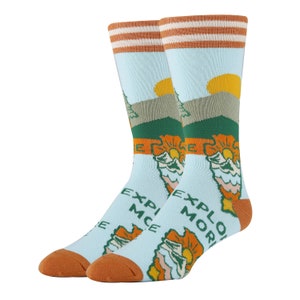 May include: A pair of blue socks with a mountain scene and the words "Explore More" and "Experience" on them. The socks have orange and white stripes at the top.