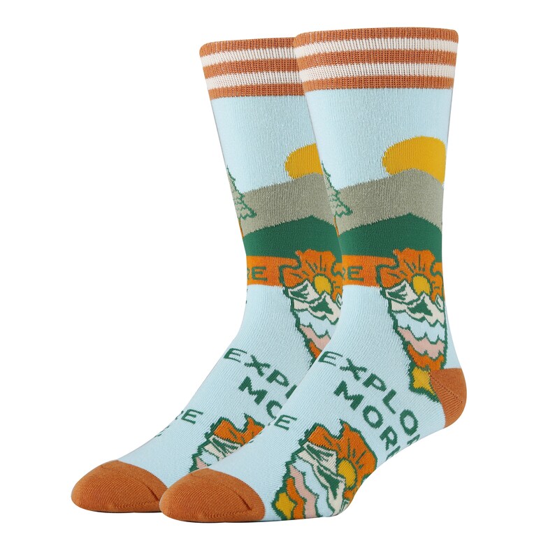 May include: A pair of blue socks with a mountain scene and the words "Explore More" and "Experience" on them. The socks have orange and white stripes at the top.