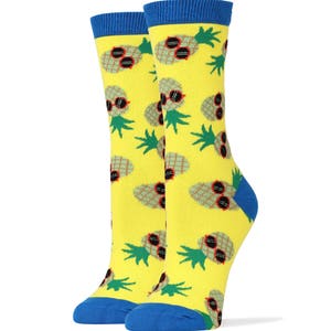 Puede incluir: Un par de calcetines amarillos con un patr&oacute;n de pi&ntilde;as que llevan gafas de sol. Los calcetines tienen pu&ntilde;os azules.