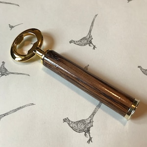 May include: A gold bottle opener with a wooden handle. The handle is made of dark wood with a striped pattern.