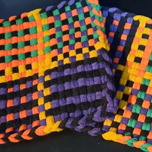 May include: Two woven pot holders in a black, orange, green and purple chequered pattern. The pot holders are handmade and have a tag that says "Thank You!"