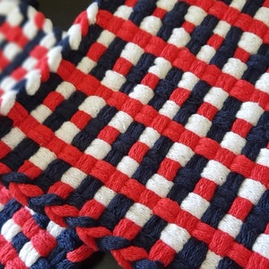 May include: Two woven pot holders in red, white and blue. The pot holders are made of thick yarn and have a square shape.