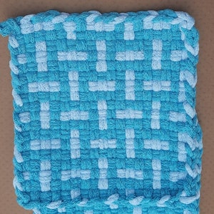 May include: A blue and white woven kitchen pot holder with a square shape and a braided border.