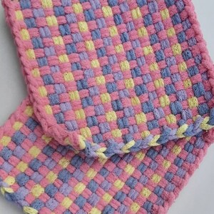 May include: Two woven pot holders in a checkered pattern with pink, yellow, and blue yarn.