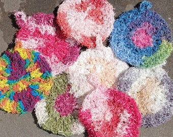 May include: A collection of eight round, textured scrubbers made from variegated yarn. Each scrubber features a small loop for hanging and displays a unique colour combination, including shades of pink, blue, green, yellow, purple, and white.