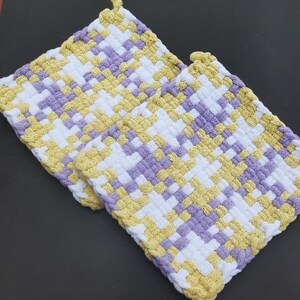 May include: Two woven pot holders in a checkered pattern of white, yellow, and purple.
