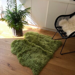 May include: A fluffy green sheepskin rug on a hardwood floor. The rug is in the shape of a heart and is placed in front of a black chair with a white sheepskin throw.
