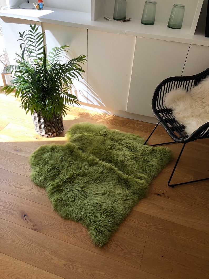 May include: A fluffy green sheepskin rug on a hardwood floor. The rug is in the shape of a heart and is placed in front of a black chair with a white sheepskin throw.