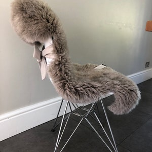 May include: A gray sheepskin chair cushion with a white bow on a chrome chair.