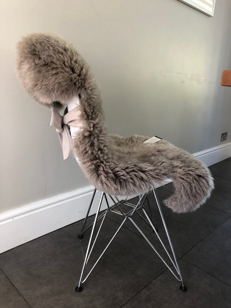 May include: A gray sheepskin chair cushion with a white bow on a chrome chair.
