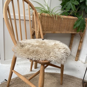 Op de afbeelding: Een houten stoel met een schapenvacht zitkussen. De stoel heeft een gebogen rugleuning en een geweven zitting. De stoel staat op een geweven tapijt.