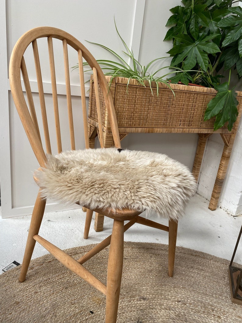 Op de afbeelding: Een houten stoel met een schapenvacht zitkussen. De stoel heeft een gebogen rugleuning en een geweven zitting. De stoel staat op een geweven tapijt.