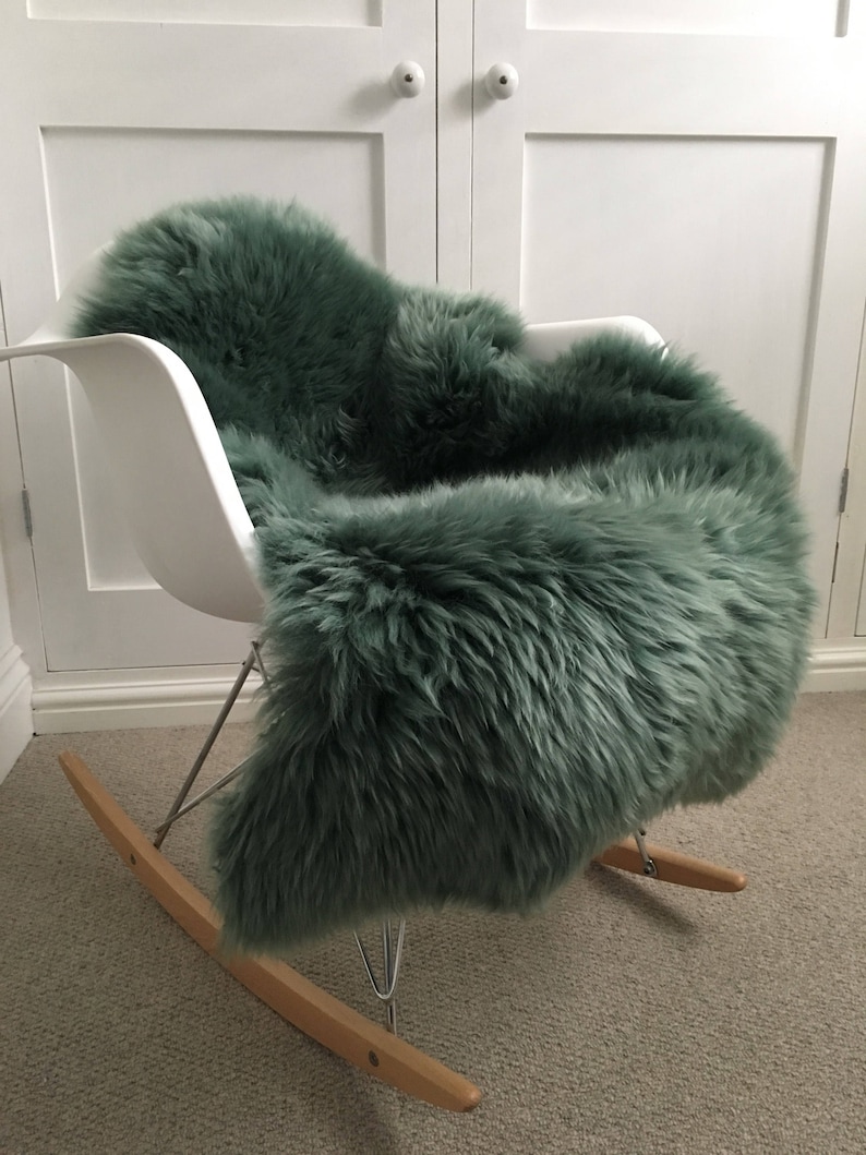 May include: A green sheepskin rug placed on a white rocking chair. The rug is soft and fluffy, and the chair is made of metal and wood.