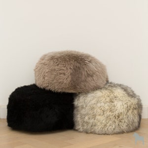 Peut inclure: Trois poufs ronds et moelleux de différentes couleurs : beige, noir et blanc. Les poufs sont empilés les uns sur les autres.