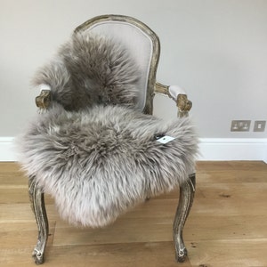 Puede incluir: Una piel de oveja de color marr&oacute;n claro drapeada sobre un sill&oacute;n de estilo vintage con un asiento de tela beige claro. La silla tiene patas talladas ornamentadas y un respaldo curvo.