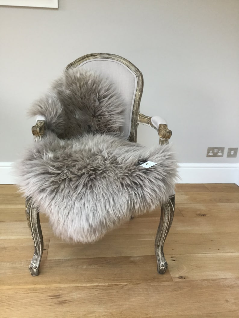 Puede incluir: Una piel de oveja de color marr&oacute;n claro drapeada sobre un sill&oacute;n de estilo vintage con un asiento de tela beige claro. La silla tiene patas talladas ornamentadas y un respaldo curvo.