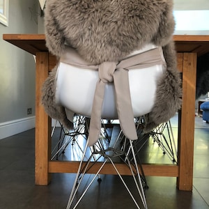 May include: A brown faux fur chair cushion with a white tie. The cushion is tied around a white chair with a chrome base.